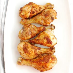 A white platter with six cooked air fryer chicken drumsticks.