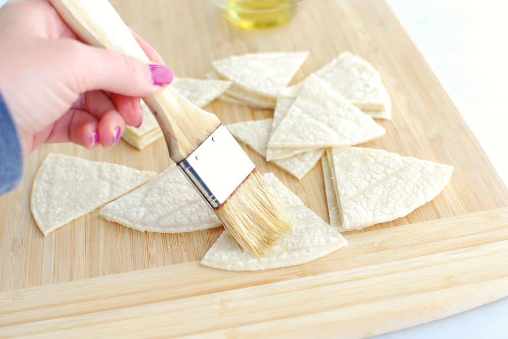 A woman holding a brush and brushing tortillas with olive oil.