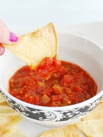 A woman dipping an air fryer tortilla chip in salsa.