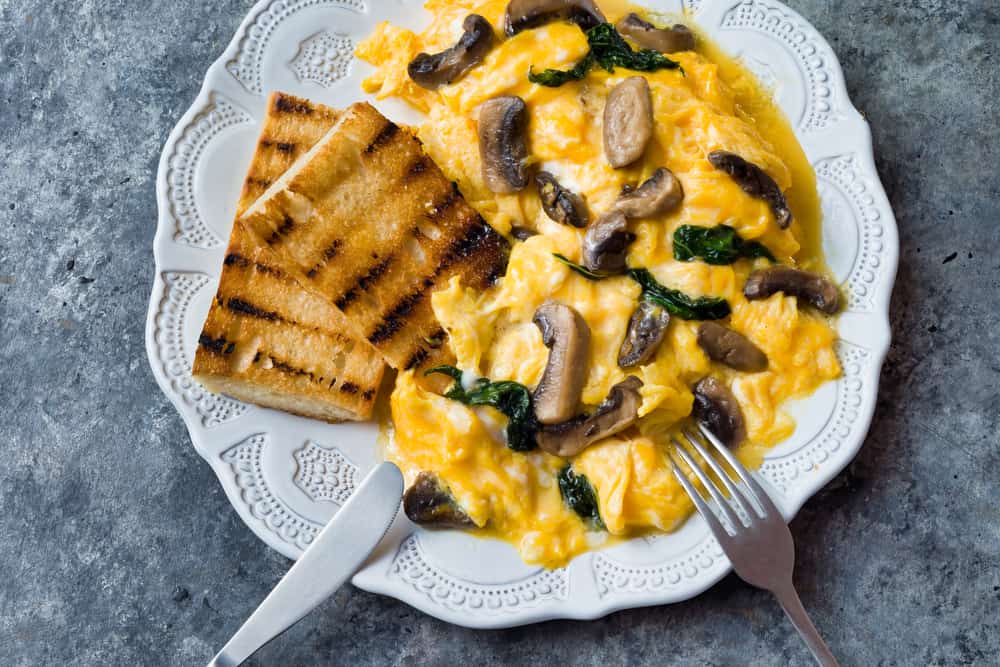 Scrambled eggs with spinach and mushrooms on a plate, along with some toast.