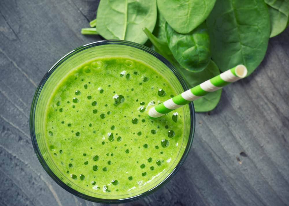 Green smoothie next to fresh spinach leaves.