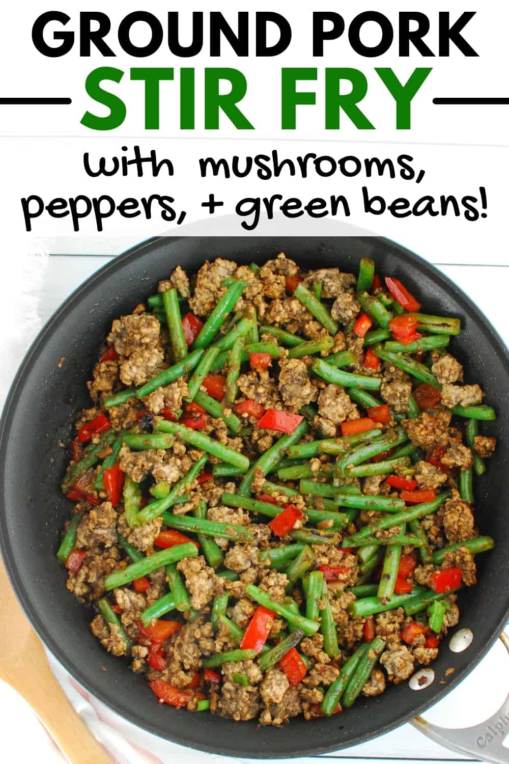 A skillet with ground pork stir fry next to a napkin and wooden spoon.