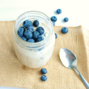 A mason jar filled with high protein overnight oats topped with blueberries.