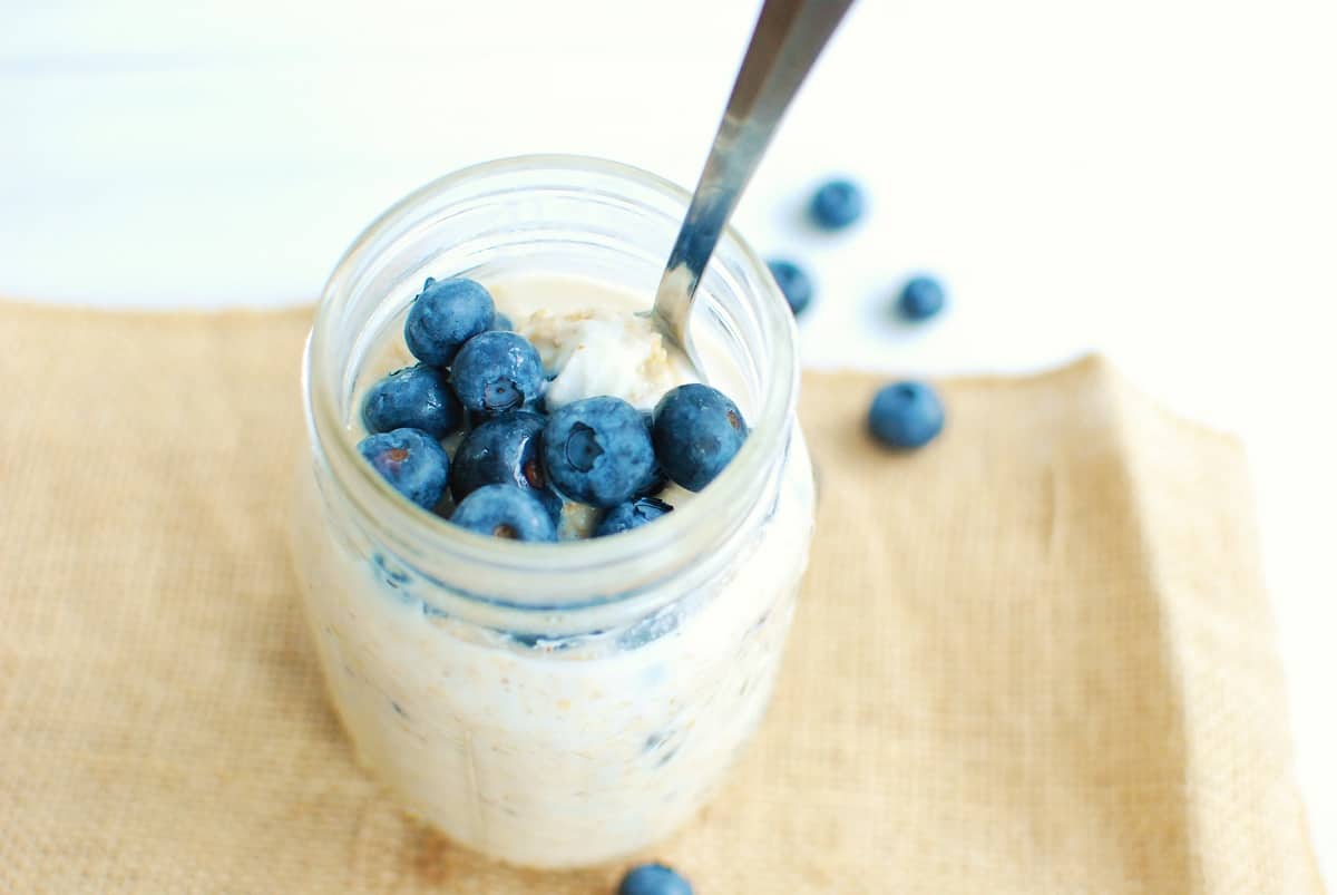 A jar of high protein overnight oats topped with blueberries with a spoon in the jar.