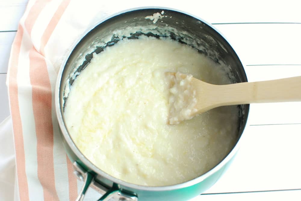 A small pot with creamy grits, and a wooden spoon.