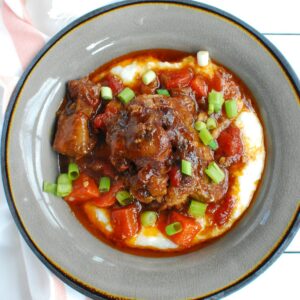 A grey bowl filled with oxtail and grits, next to a cloth napkin.