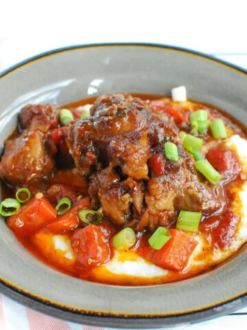 A grey bowl with oxtail and grits, along with the braising liquid stew.