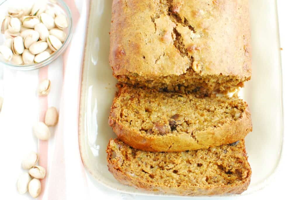 A loaf of pistachio banana bread next to some shelled pistachios.