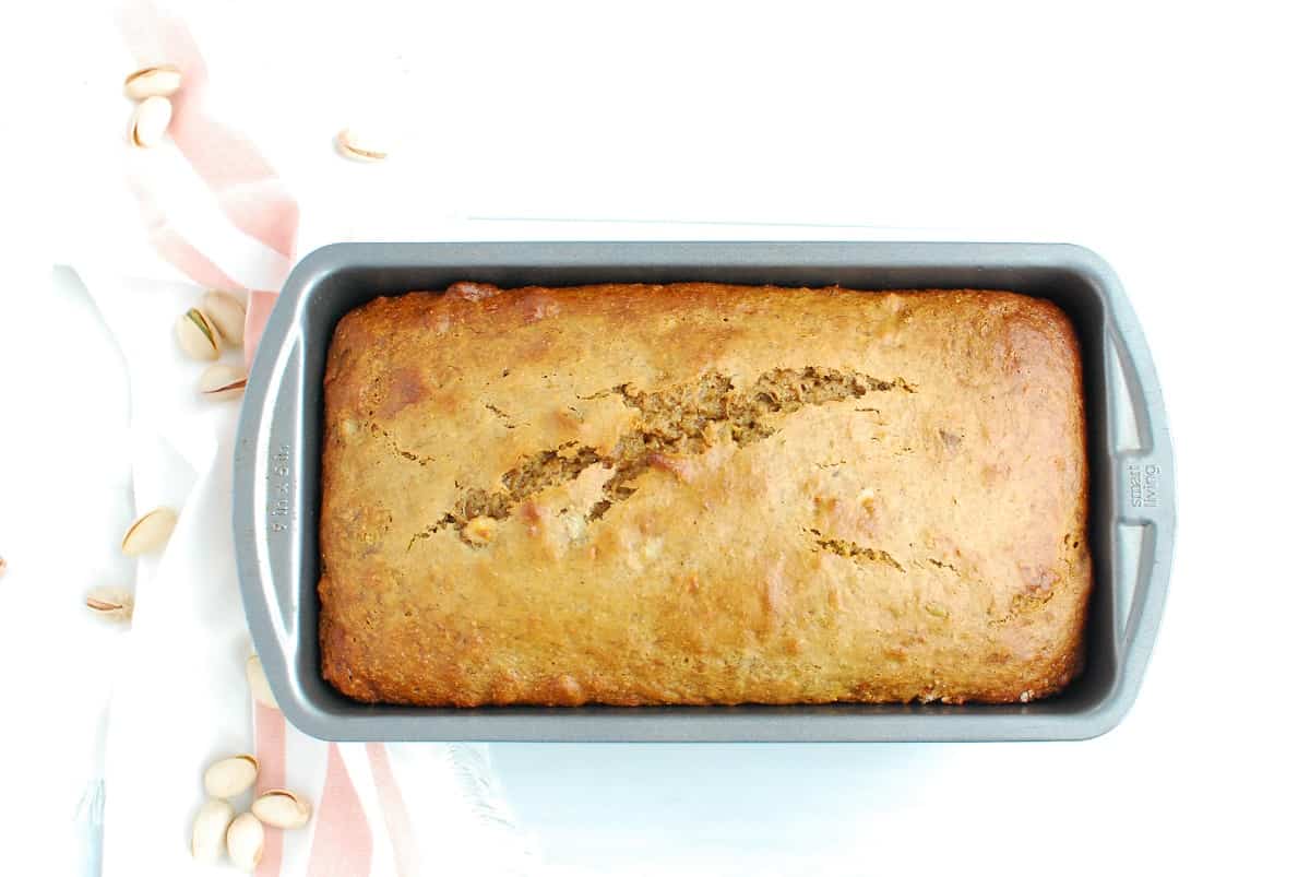 A loaf pan with a cooked loaf of pistachio banana bread.