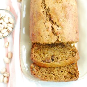 A loaf of pistachio banana bread on a plate with two slices cut.