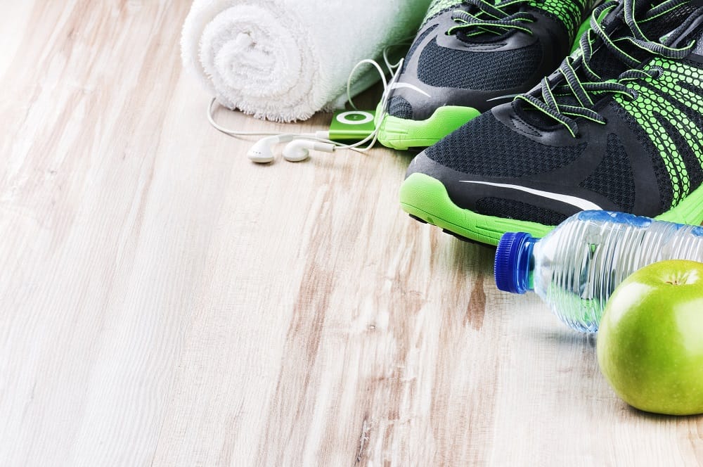 Sneakers next to headphones, a towel, a water bottle, and an apple.