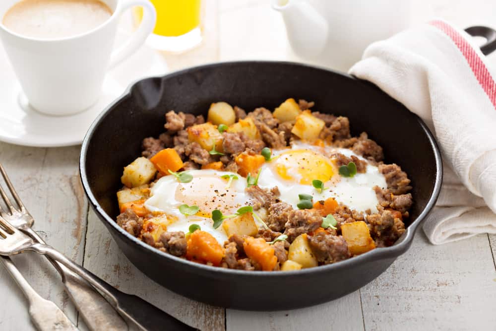 Potato and sweet potato hash with eggs in cast iron pan