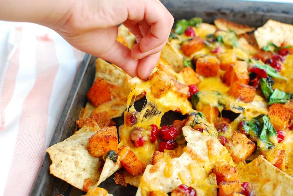 A child's hand picking up a nacho from the sheet pan.