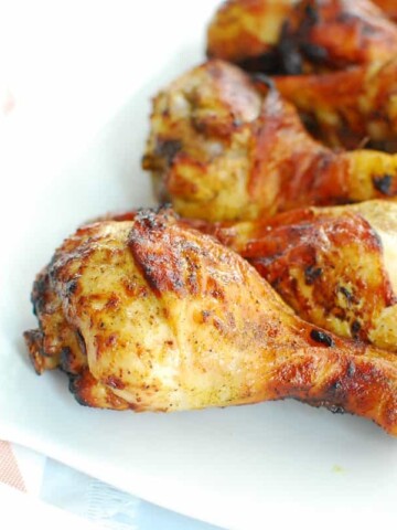 A white platter with several cooked curry chicken drumsticks.