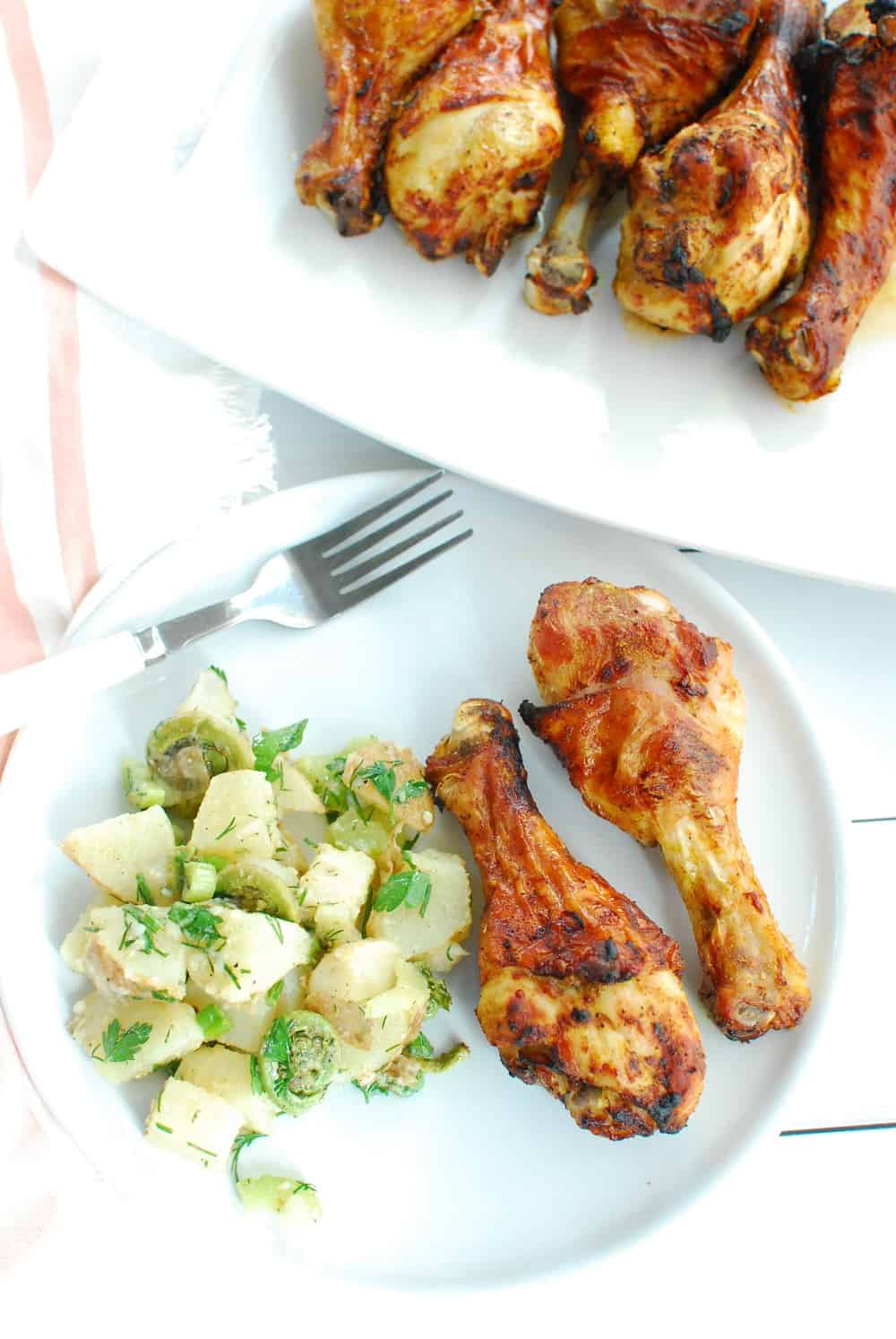 Two curry chicken drumsticks on a white plate next to herbed potato salad.