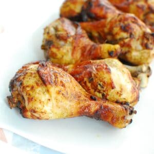 A close up of a curry seasoned chicken drumstick on a white plate.