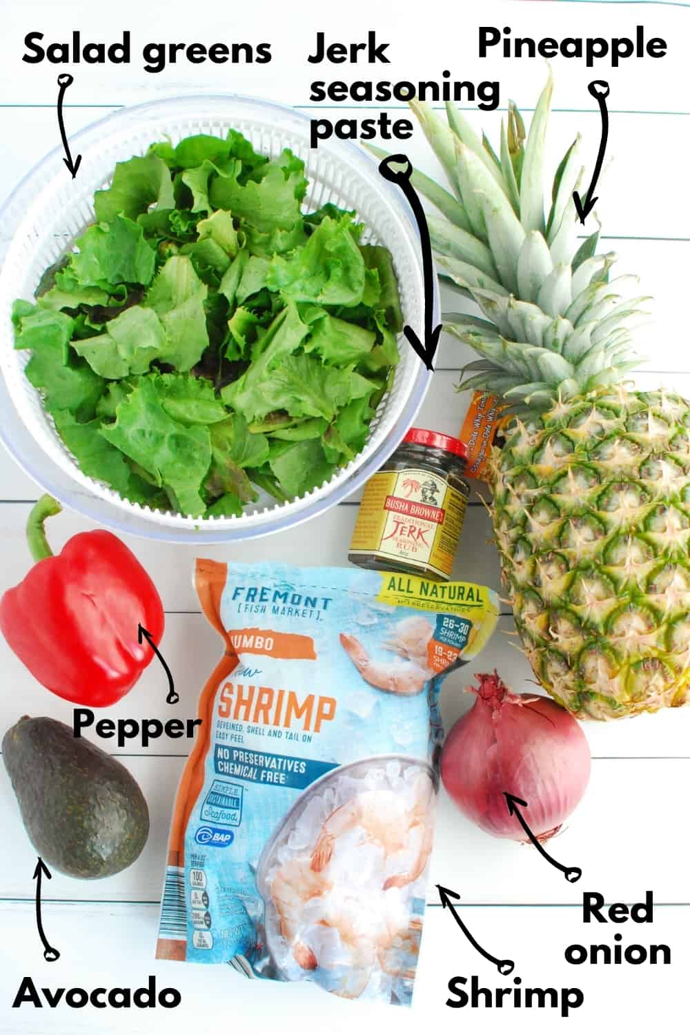 An overhead shot of all the ingredients, including lettuce, bell pepper, avocado, shrimp, jerk seasoning, red onion, and pineapple.