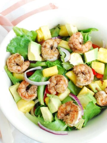 A bowl full of jerk shrimp salad next to a napkin and fork.