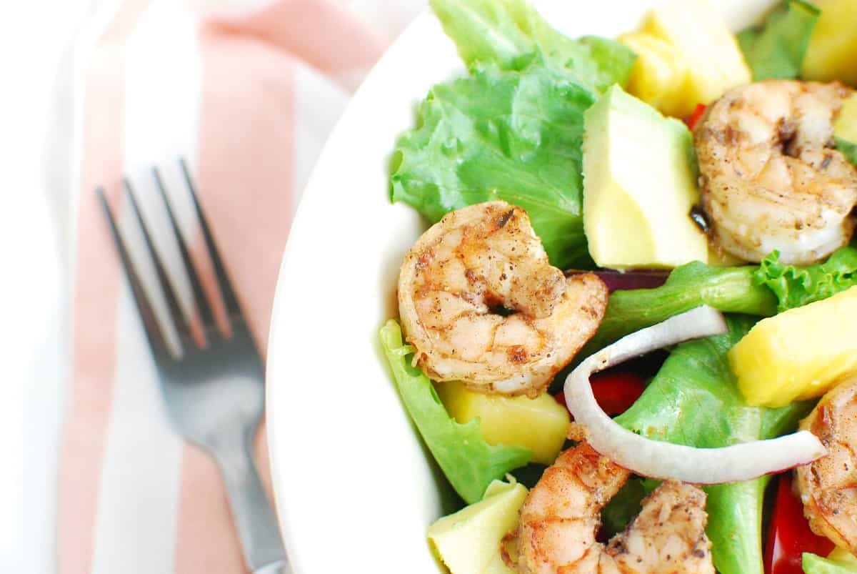 A close up of one piece of shrimp on top of salad, next to a napkin and fork.