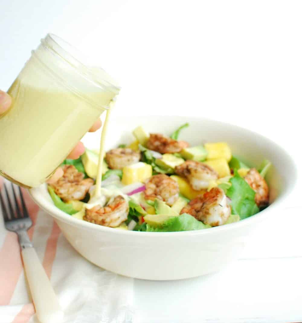 A woman pouring dressing from a jar onto a bowl of salad.