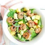 A bowl of jerk shrimp salad with lettuce, pepper, pineapple, and avocado.