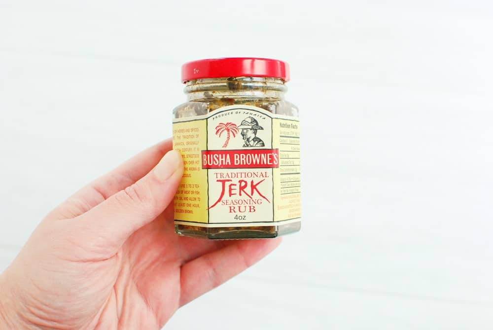 A woman's hand holding a jar of jerk seasoning paste.