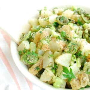 A bowl of vegan dill potato salad with fiddleheads, with a wooden spoon in the bowl.