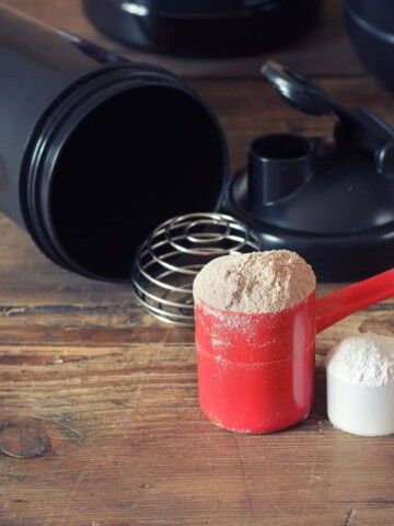 Two scoops of whey protein powder next to a shaker cup.