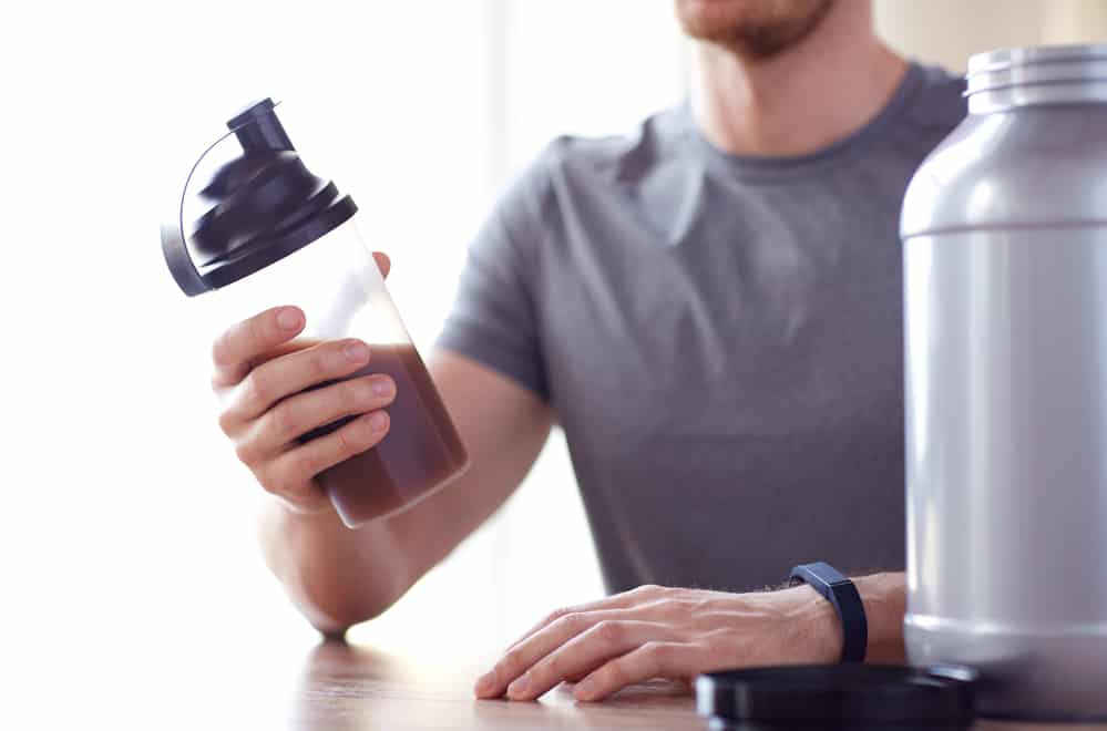 A male triathlete holding a shaker bottle with whey protein in it.