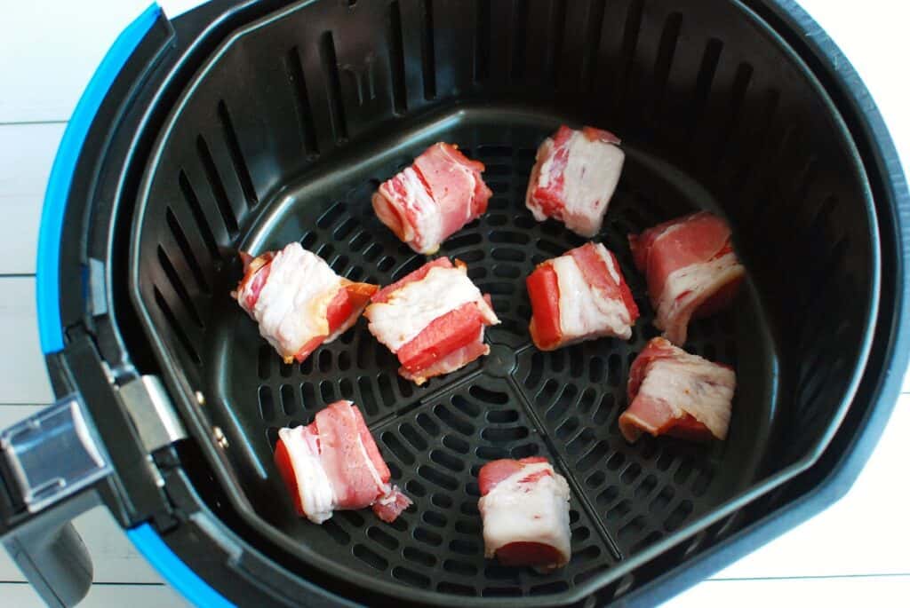 Uncooked bacon wrapped watermelon in an air fryer basket.