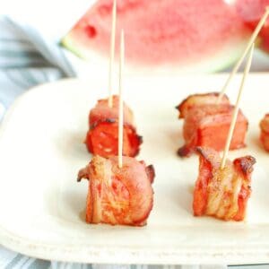 Bacon wrapped watermelon bites with toothpicks in them on a plate.