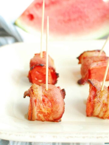 Bacon wrapped watermelon bites with toothpicks in them on a plate.