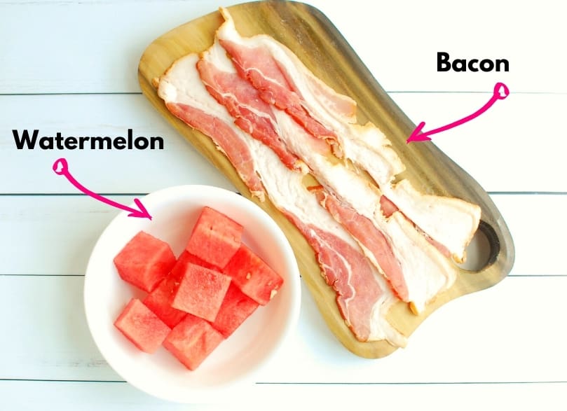 A bowl of watermelon and slices of bacon on a white table.