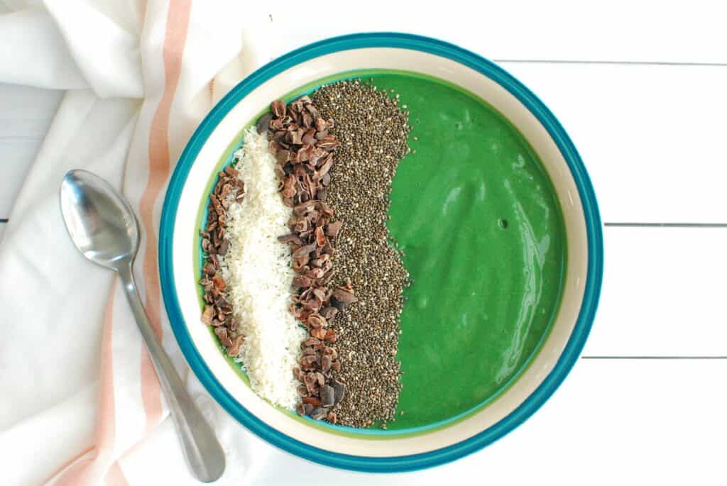 An overhead shot of a spirulina smoothie bowl topped with chia seeds, coconut, and cacao nibs.