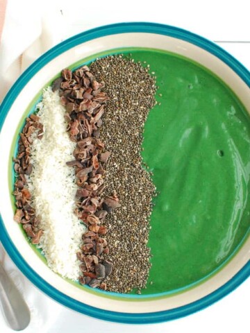 An overhead shot of a spirulina smoothie bowl topped with chia seeds, coconut, and cacao nibs.