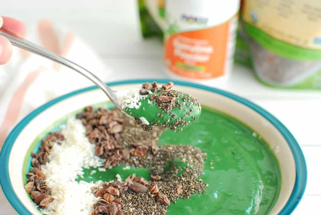 A woman's hand holding a spoon with spirulina smoothie on it.