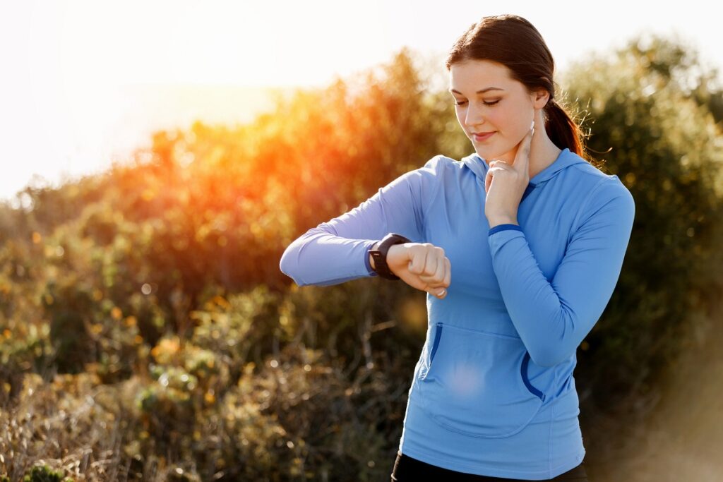 A woman checking her heart rate during a run on a sunny day.