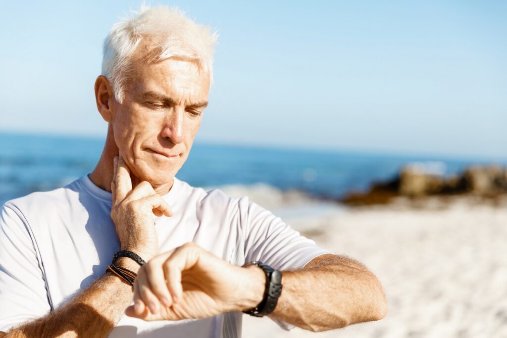 An older man checking his heart rate during a run on the beach.