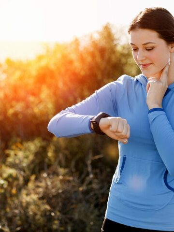 A woman checking her heart rate during a run on a sunny day.