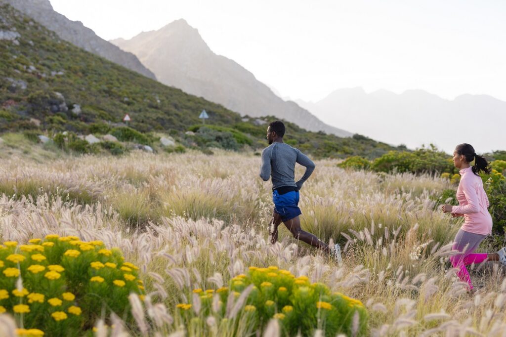 Two runners outside in a field running towards a mountain.