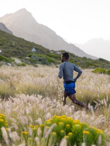 Two runners outside in a field running towards a mountain.