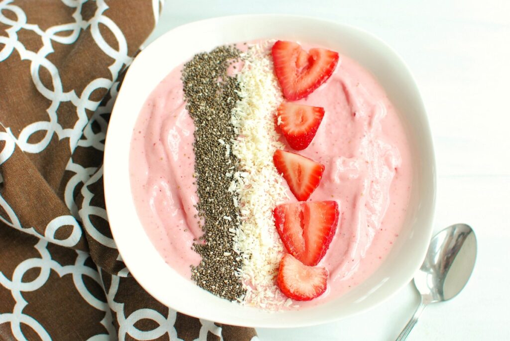 A banana strawberry smoothie bowl topped with chia seeds, berries, and coconut.