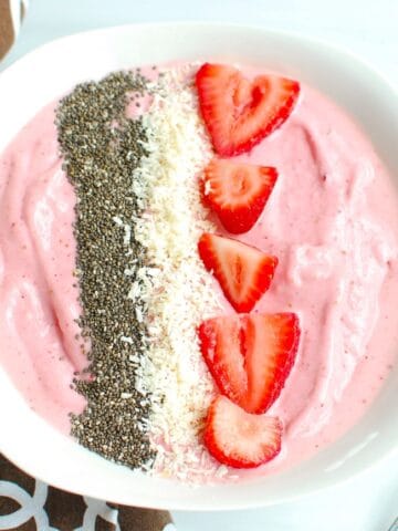 A strawberry banana smoothie bowl topped with chia seeds, coconut, and strawberries.