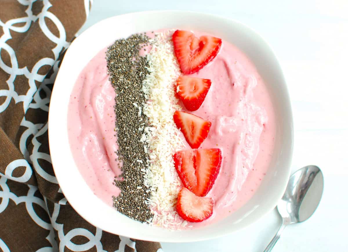 A strawberry banana smoothie bowl topped with chia seeds, coconut, and strawberries.