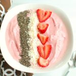 A strawberry banana smoothie bowl next to a brown napkin and a spoon.