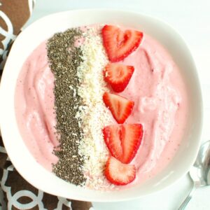 A strawberry banana smoothie bowl next to a brown napkin and a spoon.