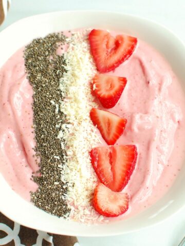 A strawberry banana smoothie bowl next to a brown napkin and a spoon.