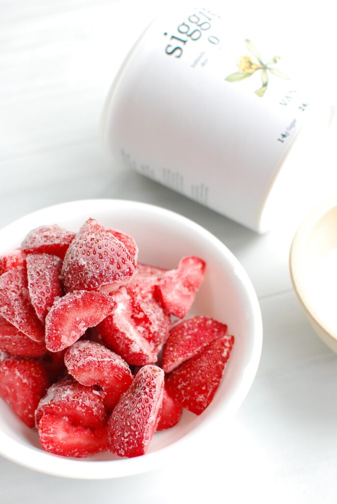 Frozen strawberries in a bowl next to a container of yogurt.