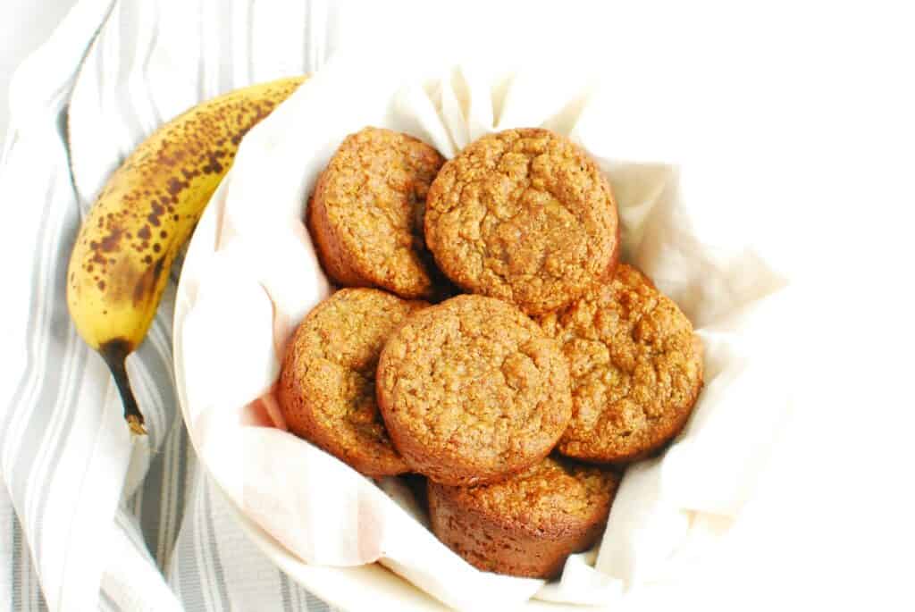 A bowl of banana muffins next to a napkin and overripe banana.