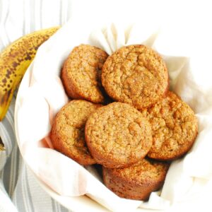 A bowl lined with a napkin filled with almond flour banana muffins.